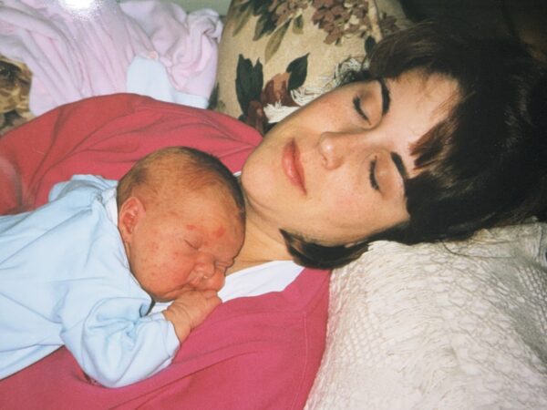 A young mother lays on a sofa with her infant daughter sleeping on the mother's chest.