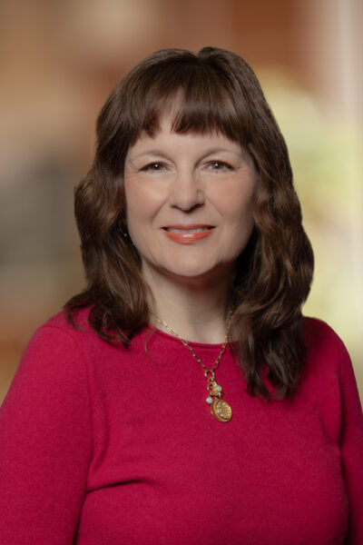 Laura Munkel, MD, a woman with dark shoulder-length hair wearing a bright pink top and necklace.