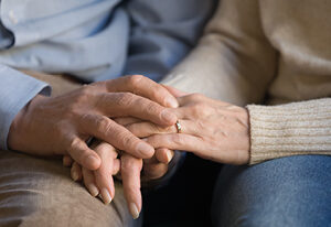 Close up of a couple sitting side-by-side, focusing just on their interlocking hands.