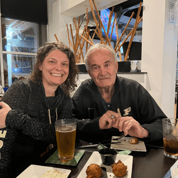 Two people sit together and lean close at a restaurant table with drinks and appetizers.