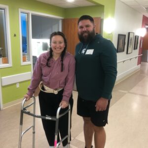 Taylor Harbin uses a walker while standing with Andrew Harbin in a Beacon Kalamazoo hallway during recovery in May 2025.